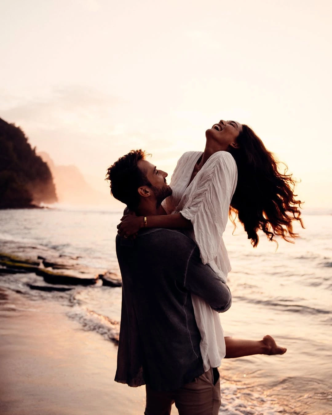 Couple laughing together on a beach at sunset